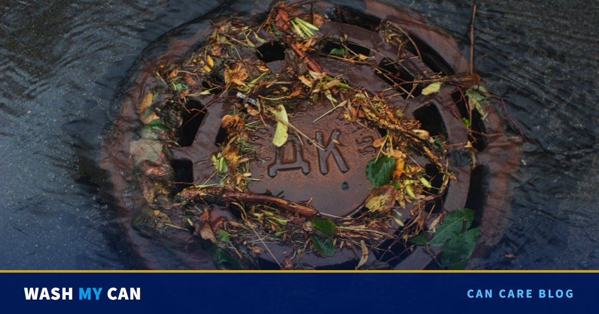 A round storm drain covered in wet leaves, twigs and debris, with rainwater swirling over the street around it