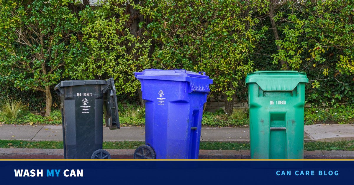 Black, blue and green trash and recycling cans lined up at the curb in front of a green hedge